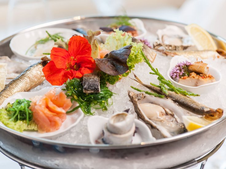 Fisch, Meeresfrüchte, Zitronenscheiben, Salat-, und Blumendeko teilweise in kleinen Schüsseln angerichtet auf crushed Eis in einer größeren Edelstahlschüssel