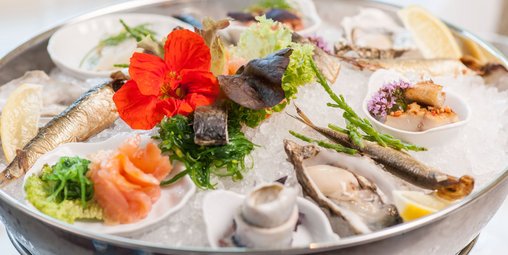 Fisch, Meeresfrüchte, Zitronenscheiben, Salat-, und Blumendeko teilweise in kleinen Schüsseln angerichtet auf crushed Eis in einer größeren Edelstahlschüssel
