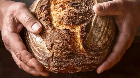 Person hält Brotlaib mit beiden Händen fest, Bildausschnitt nur Hände und Brot in der Mitte